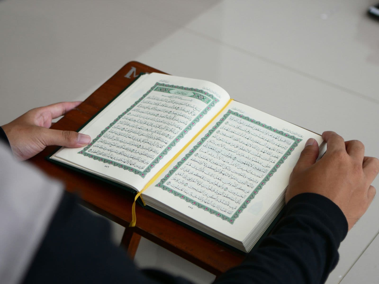 Hands resting on an open Quran on a wooden stand