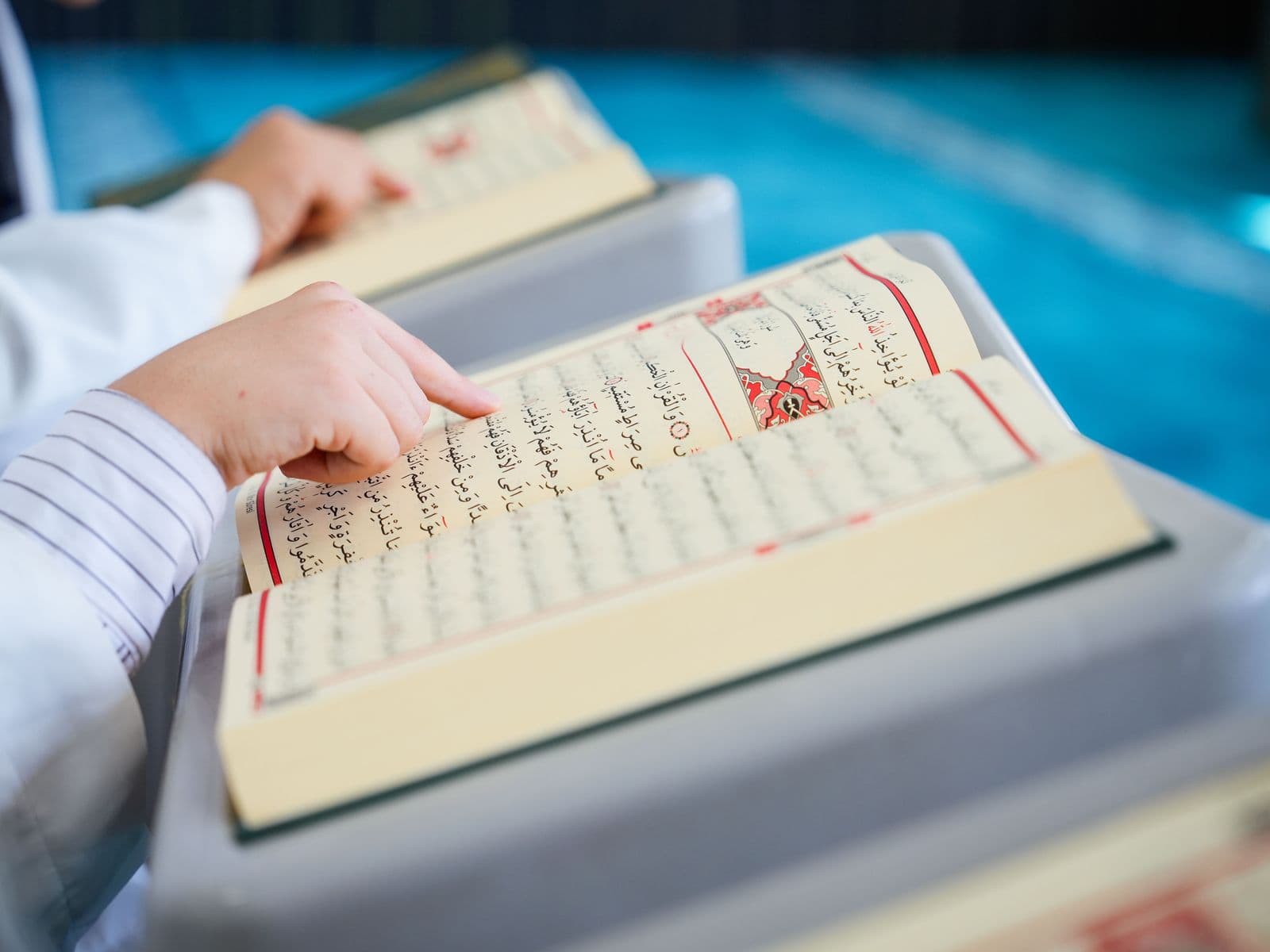 A child following the Arabic text of the Quran with a finger